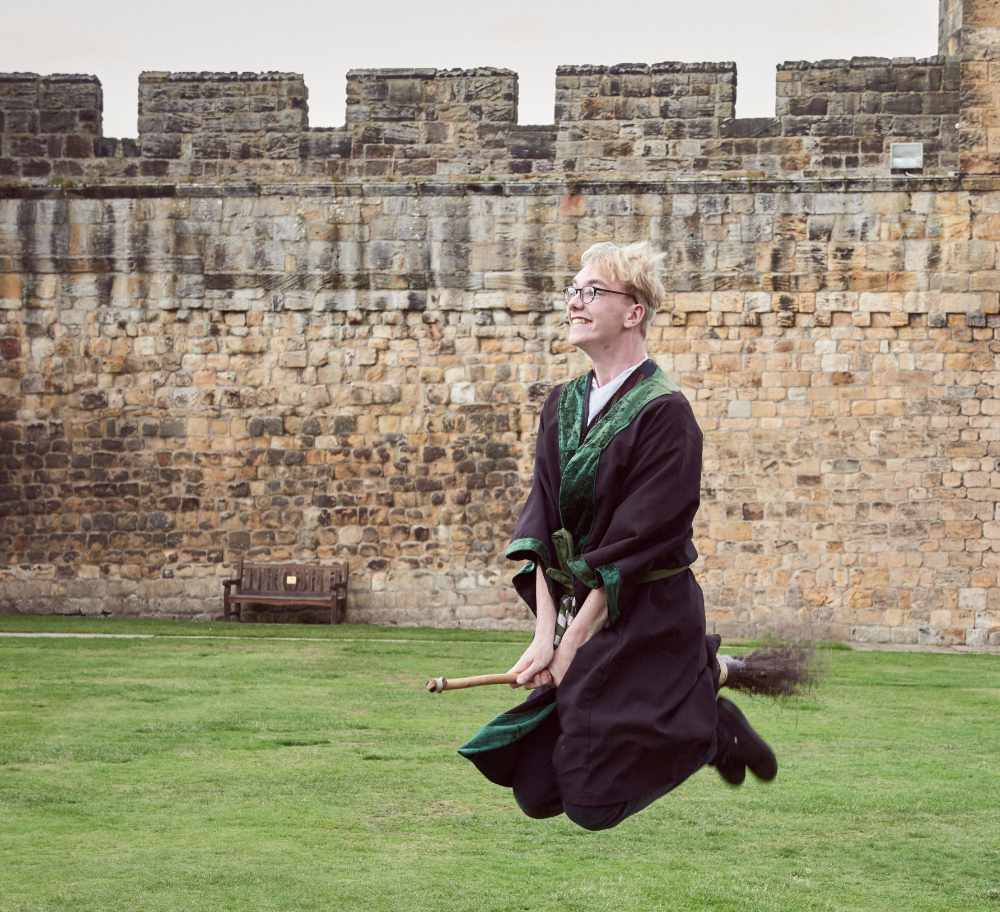 Young Man Wearing Robe And Glasses Hovering On Broomstick.